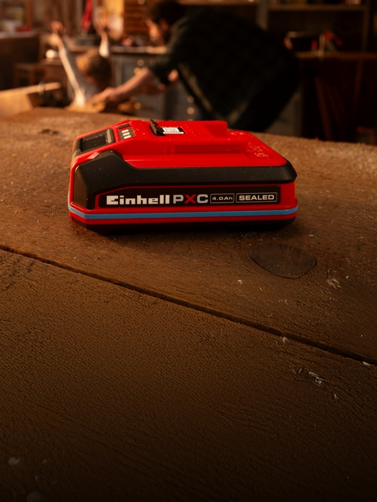 Einhell Power X-Change 4,0 Ah SEALEAD-batteri på en arbeidsbenk i tre, med blå ring og synlig etikett.