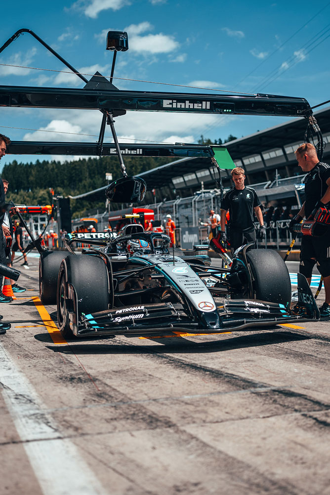 En Mercedes-AMG Formel 1-bil står i depotet, omgitt av teammedlemmer under en Einhell-garasjekonstruksjon.