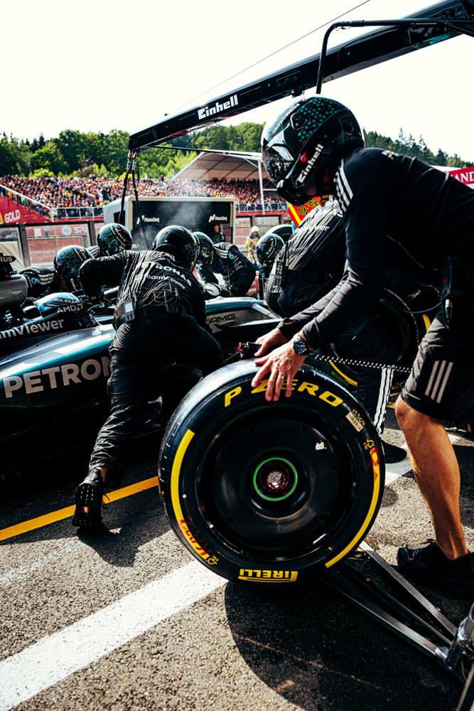 Mekanikere fra Mercedes-AMG PETRONAS Formula One Team utfører et pitstopp. Et teammedlem forbereder et Pirelli-dekk mens andre arbeider på bilen. Einhell-logoen er synlig på utstyret over bilen.
