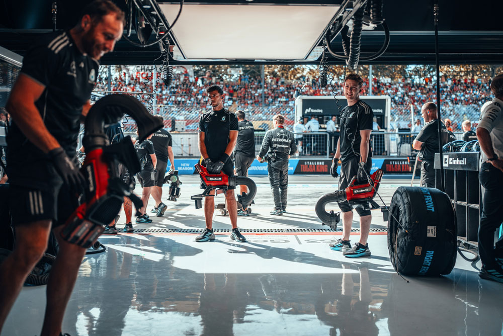 Mekanikere fra Mercedes-AMG PETRONAS Formula One Team forbereder seg i garasjen med trådløse blåsemaskiner fra Einhell før et pitstopp. I bakgrunnen er tribunene fylt med fans.