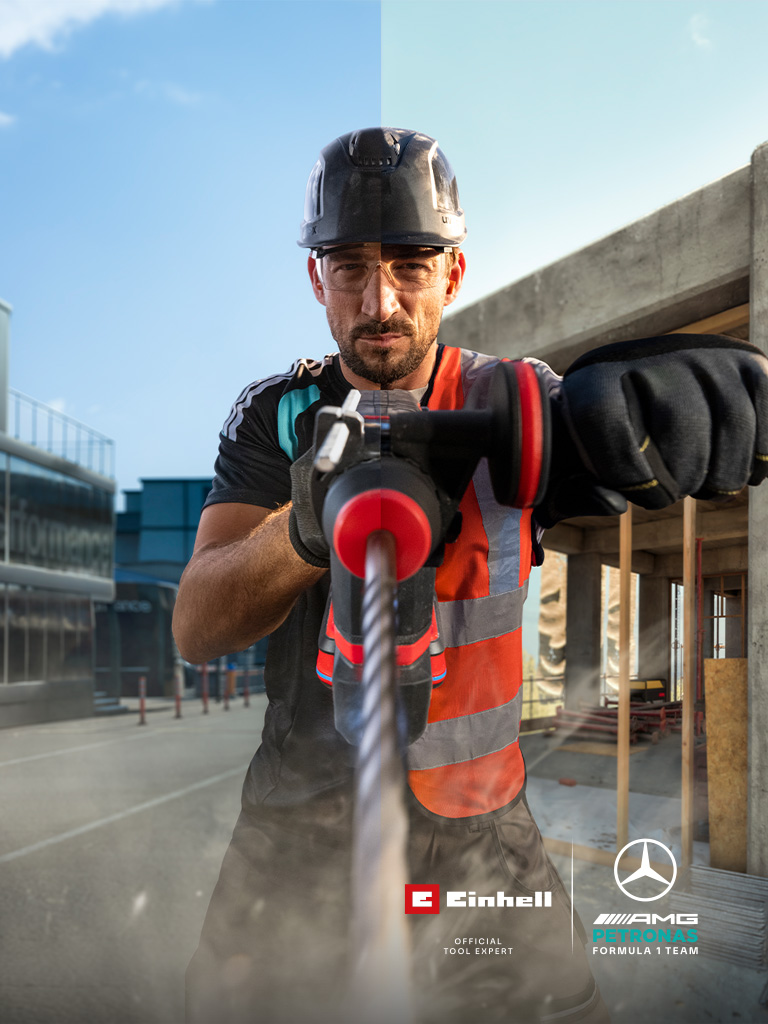 A mechanic in protective gear drilling with a power tool at a construction site.