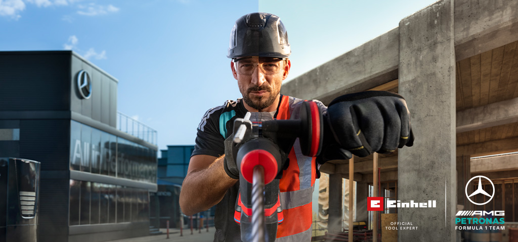 A mechanic in protective gear drilling with a power tool at a construction site.