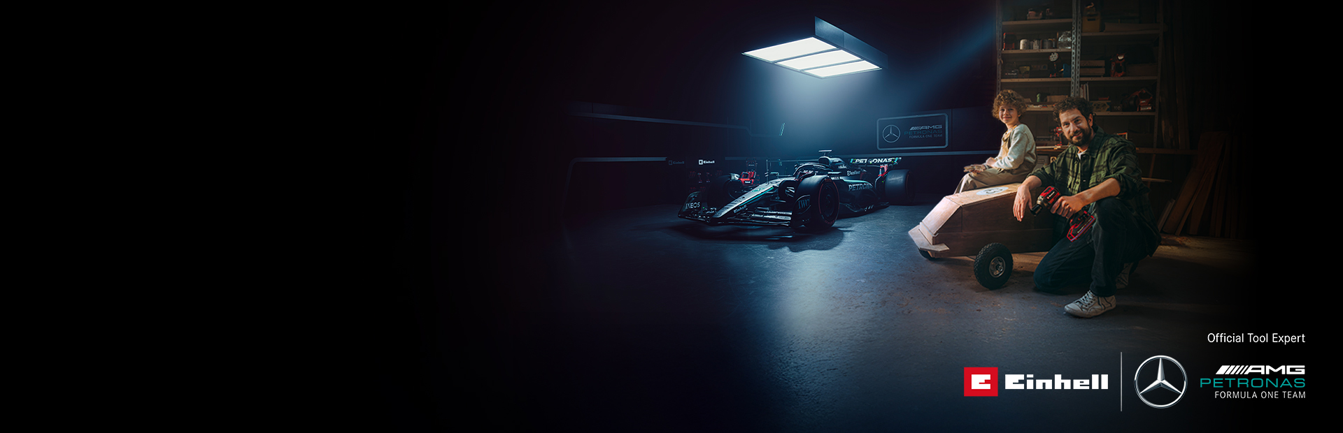 En far og et barn i et verksted med en hjemmelaget såpekassebil. I bakgrunnen sees en Mercedes-AMG PETRONAS Formel 1-bil og verktøy fra Einhell.