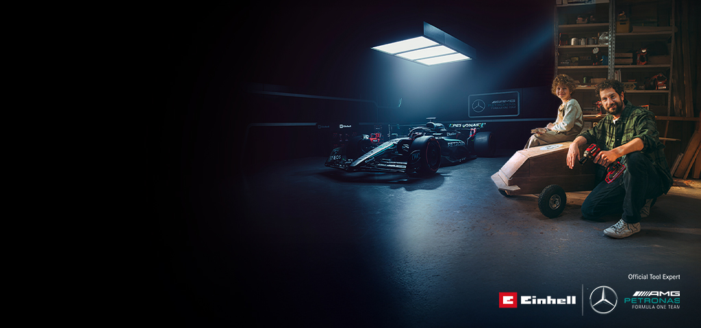 En far og et barn i et verksted med en hjemmelaget såpekassebil. I bakgrunnen sees en Mercedes-AMG PETRONAS Formel 1-bil og verktøy fra Einhell.