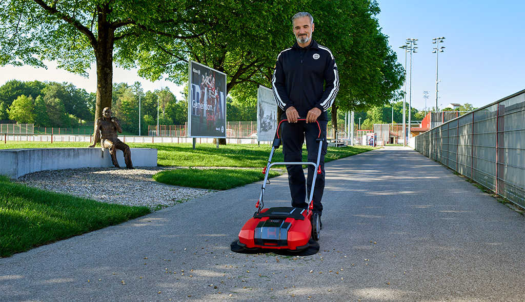 A man with a sweeper sweeps away leaves on the sidewalk